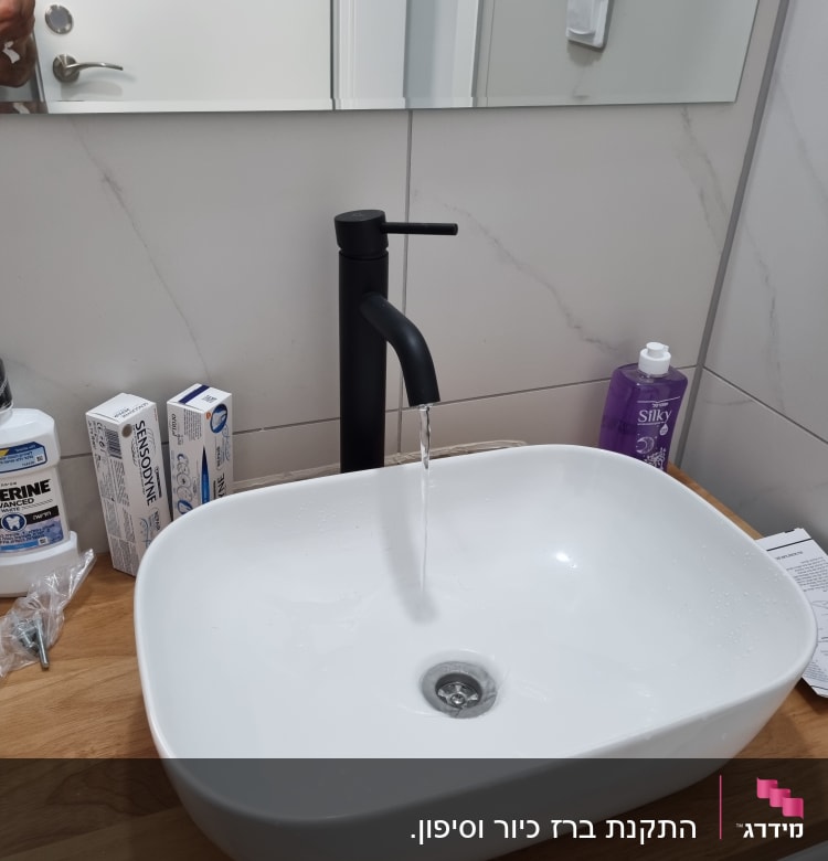 כיור עם ברז שחור זורם על משטח עץ
